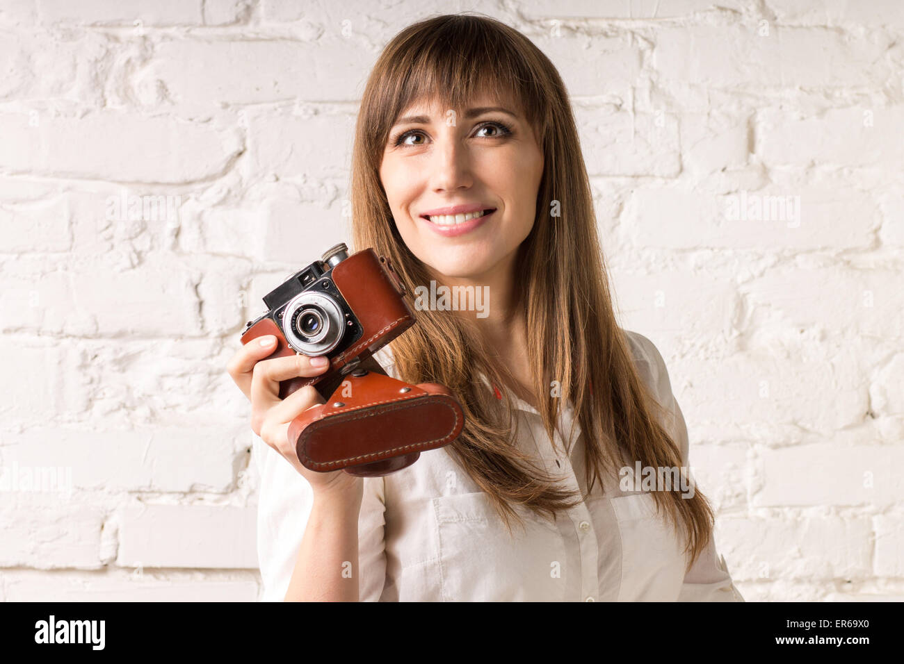 Ziemlich lächelnde Frau mit alten Filmkamera auf weißen Mauer. Fröhliches europäischen Mädchen Spaß im Studio mit Fotokamera Stockfoto