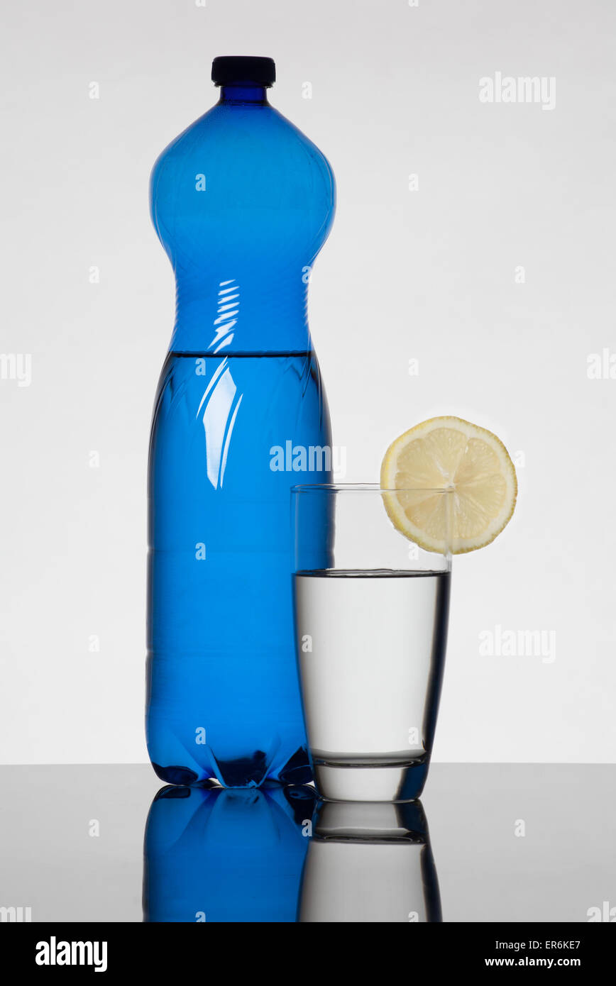 Blaue Wasser-Flasche und Glas mit Wasser gefüllt und dekoriert mit Zitrone Stockfoto