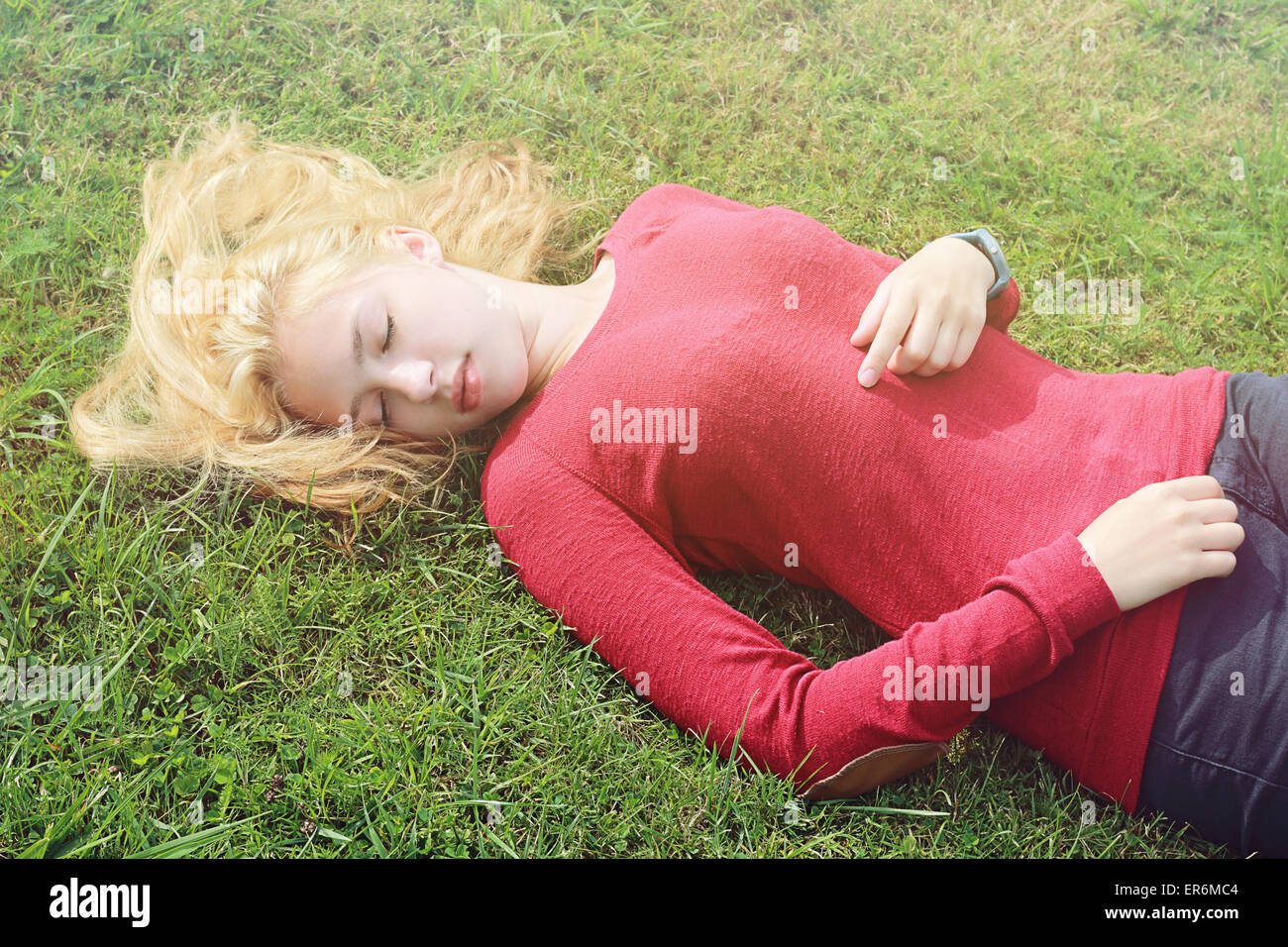 Junges Mädchen mit langen blonden Haaren auf dem Rasen liegend Stockfoto