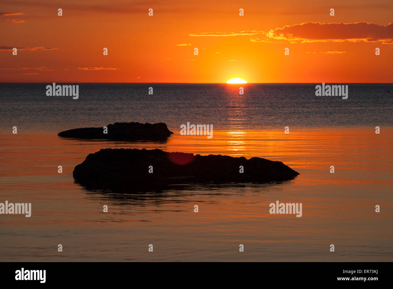 Lebendige orange Sonnenuntergang über dem Wasser, mit Rock-Silhouetten. Stockfoto