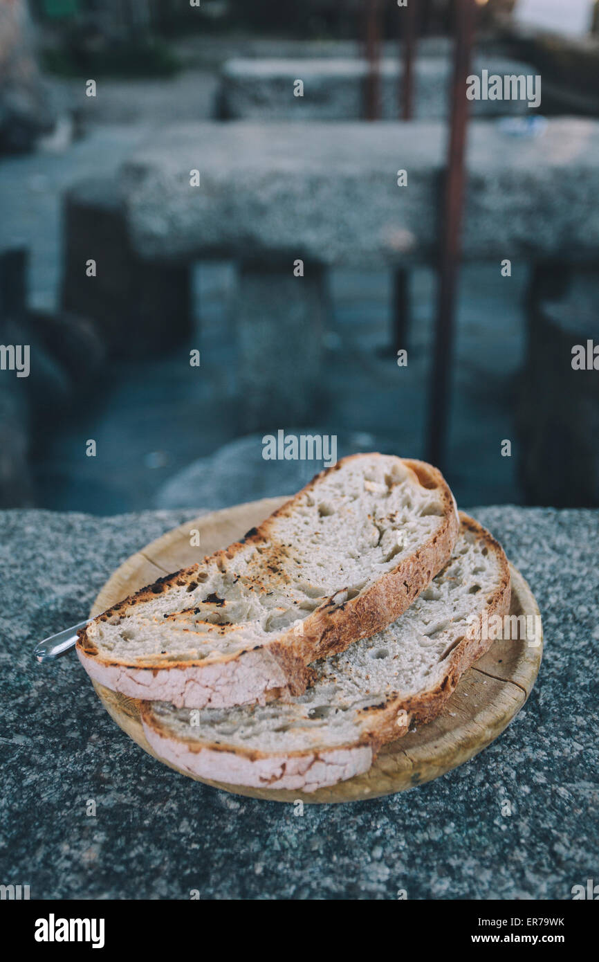 Zwei Scheiben dick geröstetes Brot sitzen auf einer Holzplatte auf einem Steintisch in Spanien. Stockfoto
