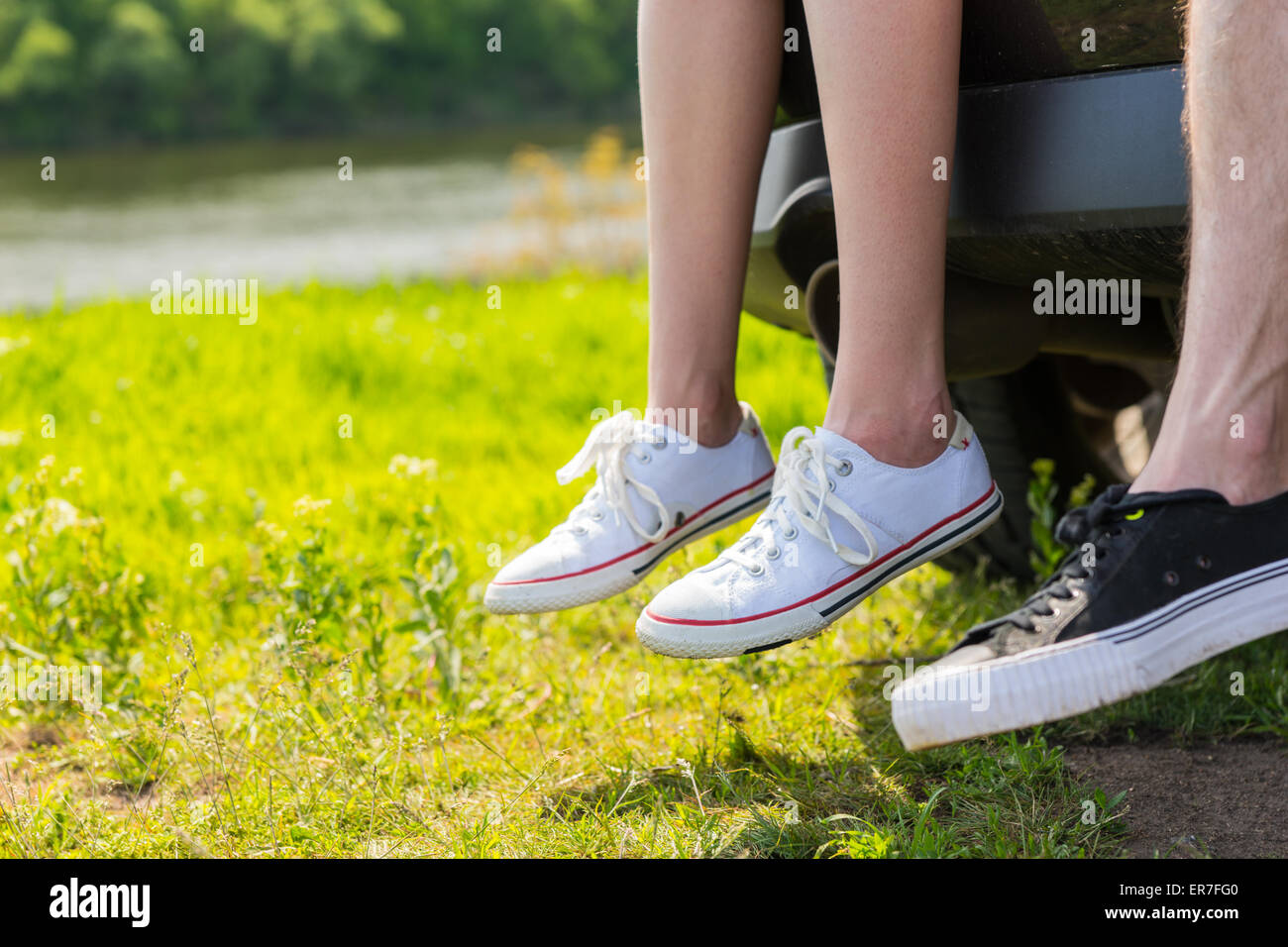 Nahaufnahme des Paares tragen Turnschuhe auf hinten Heckklappe des einsamen Fluss im grünen Wiese geparkten Fahrzeug sitzen Stockfoto
