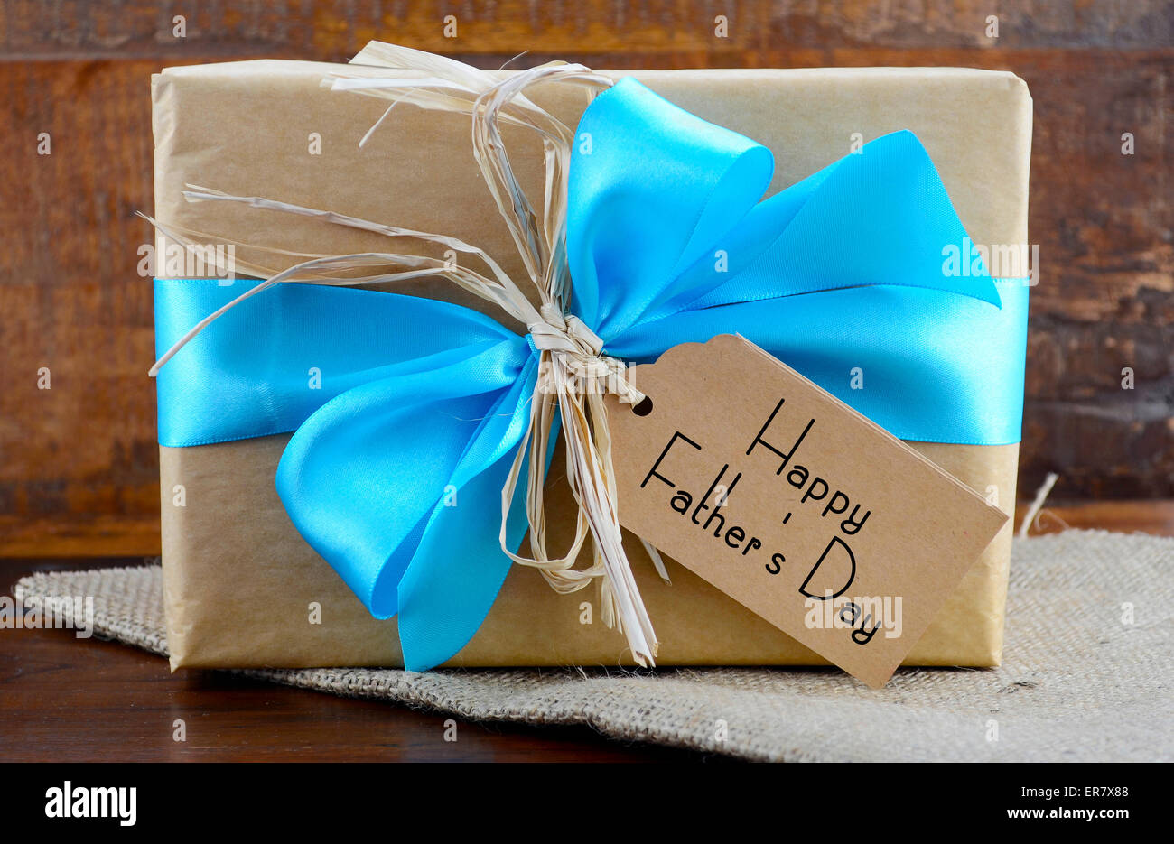 Happy Fathers Day natürliche Kraftpapier umwickelt Owith blass blau Geschenkband auf dunklem Holz. Stockfoto