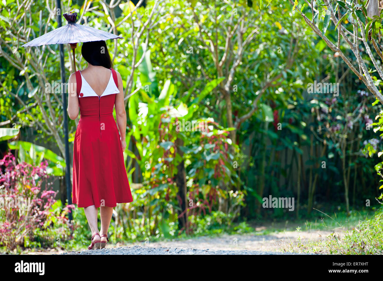Schöne Frau im roten Kleid, die durch eine Thai Garten Stockfoto