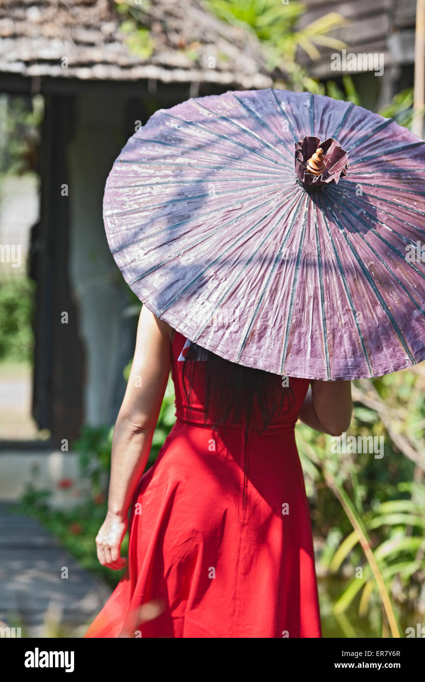 Schöne Frau im roten Kleid, die durch eine Thai Garten Stockfoto