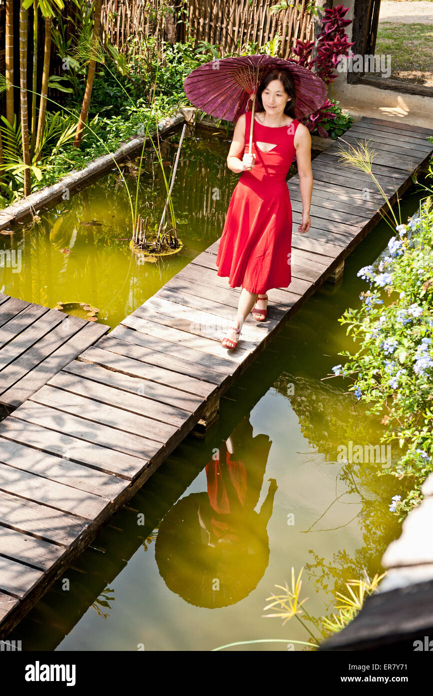Schöne Frau im roten Kleid, die durch eine Thai Garten Stockfoto