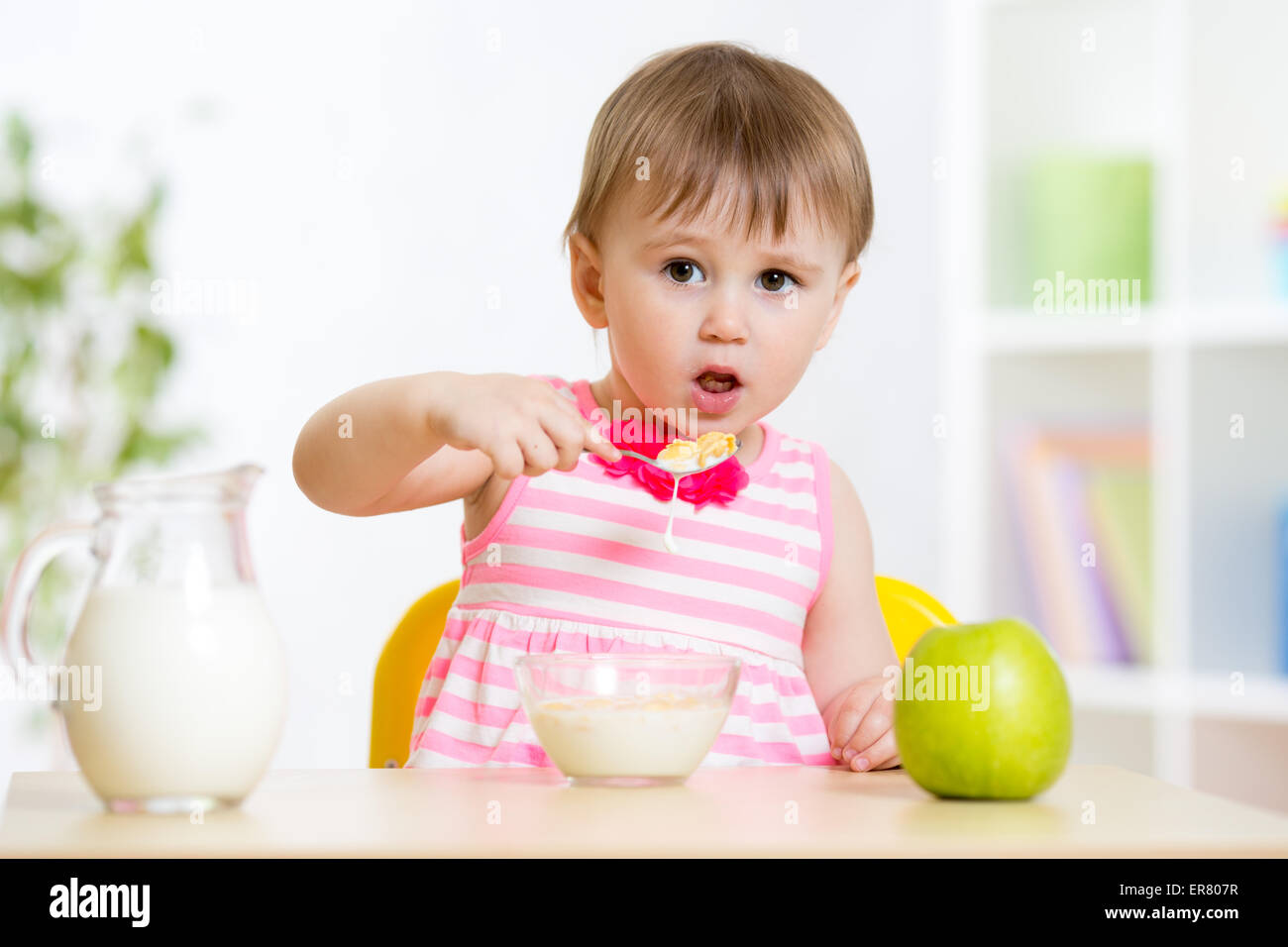 Kleine Mädchen essen Cornflakes mit Milch am Tisch im Haus Stockfoto