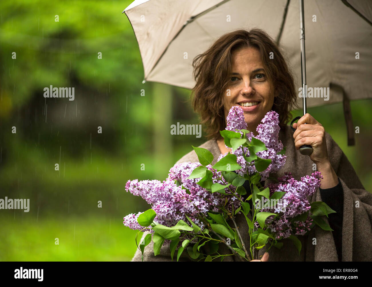 Junge schöne Frau unter einem Sonnenschirm mit einem Bouquet von Flieder in der Hand bei Regen. Stockfoto