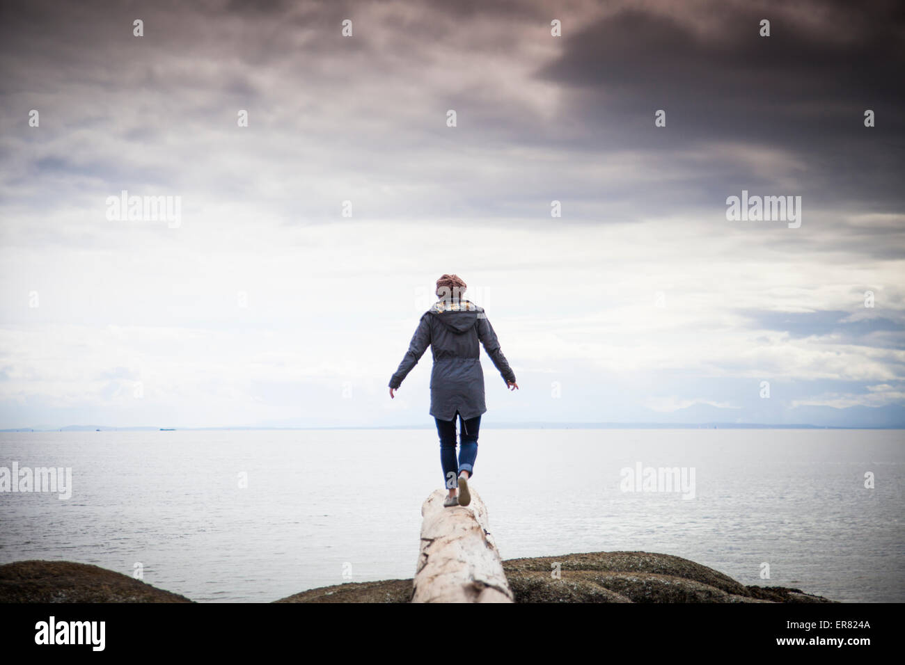 Eine junge Frau balanciert auf einem Baumstamm mit Blick auf den Pazifischen Ozean. Stockfoto