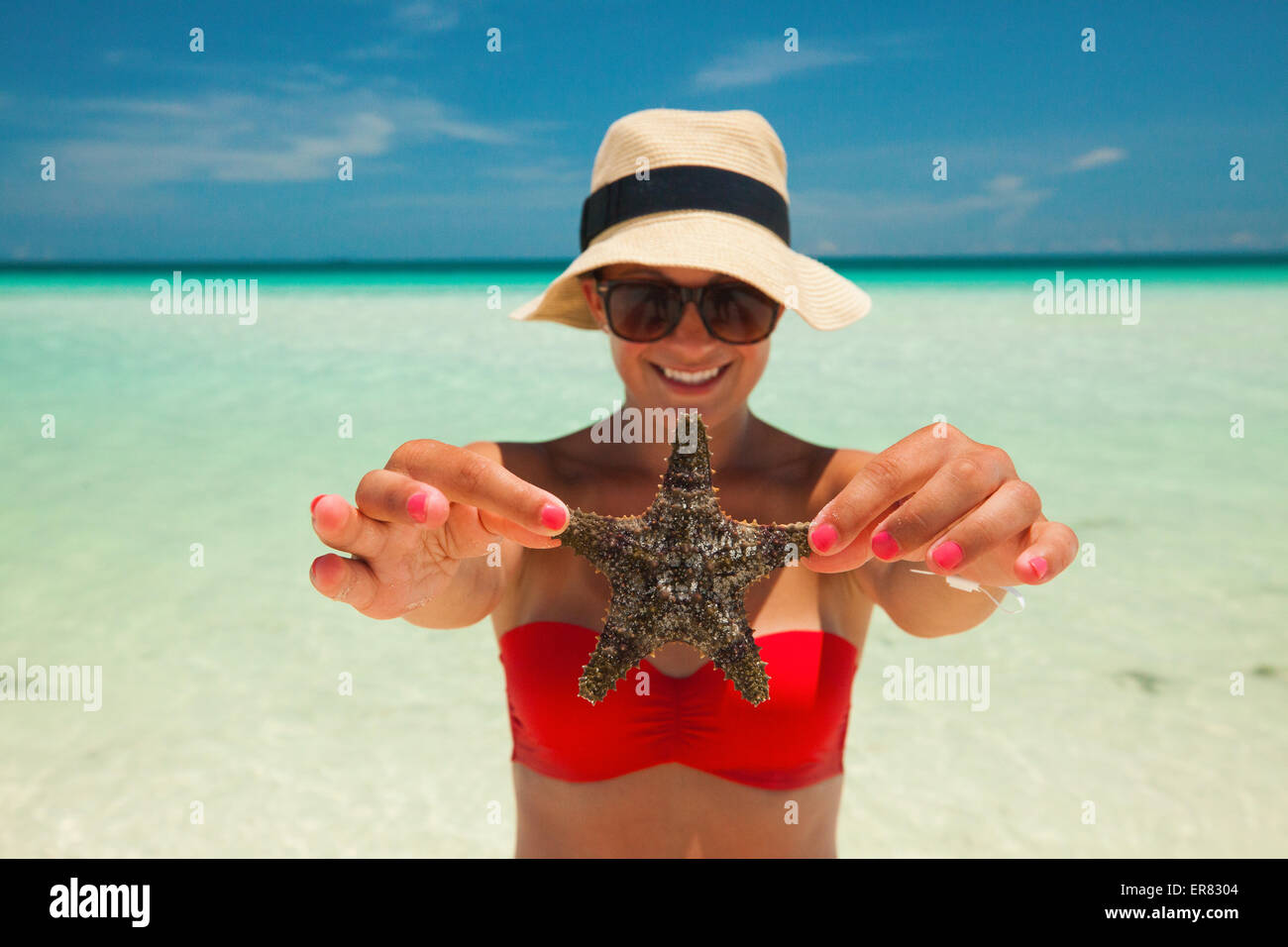 Eine junge Frau hält einen Seestern am Strand. Stockfoto