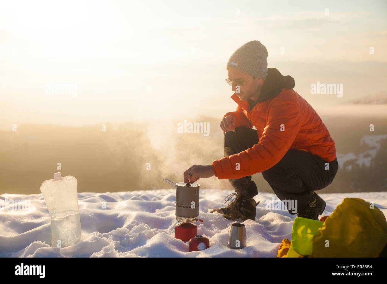 Ein Bergsteiger kümmert sich um seinen kochenden Ofen beim camping in den Bergen. Stockfoto