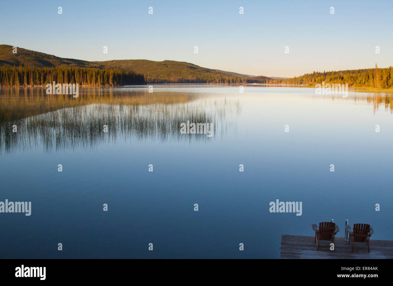 Zwei Stühle auf einem Dock blicken auf einen ruhigen See in British Columbia, Kanada. Stockfoto