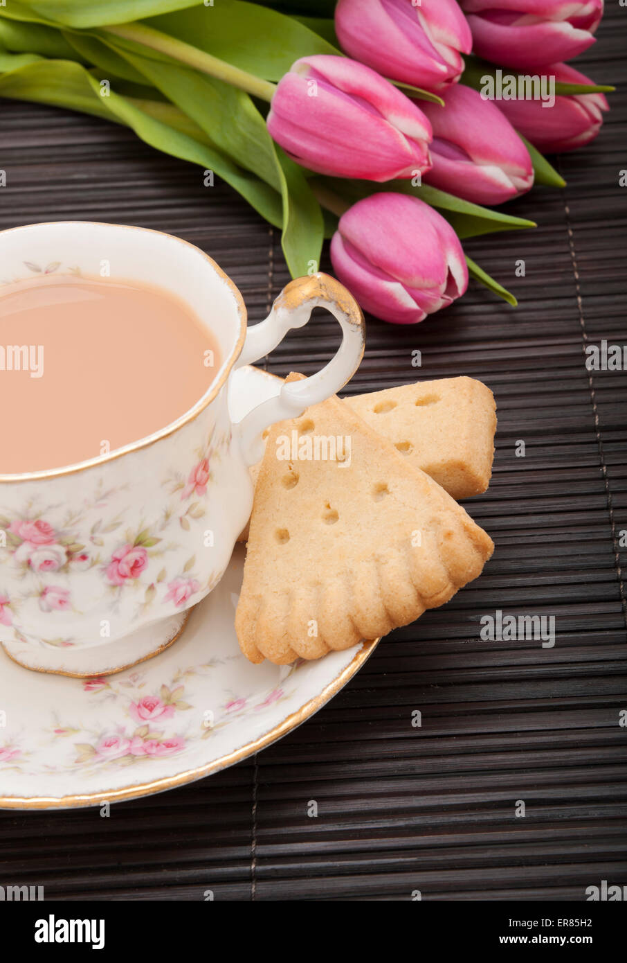 Nahaufnahme einer Tasse Tee mit Milch und einem Teller mit Keksen auf einem Tisch Stockfoto