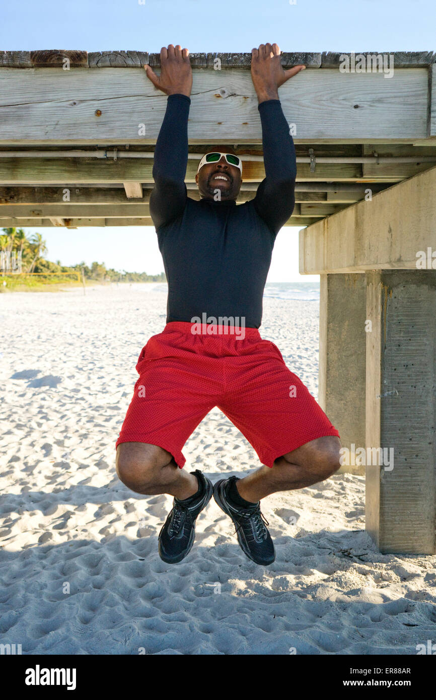Mann tut Pull Ups auf einem Beach Pier Stockfoto