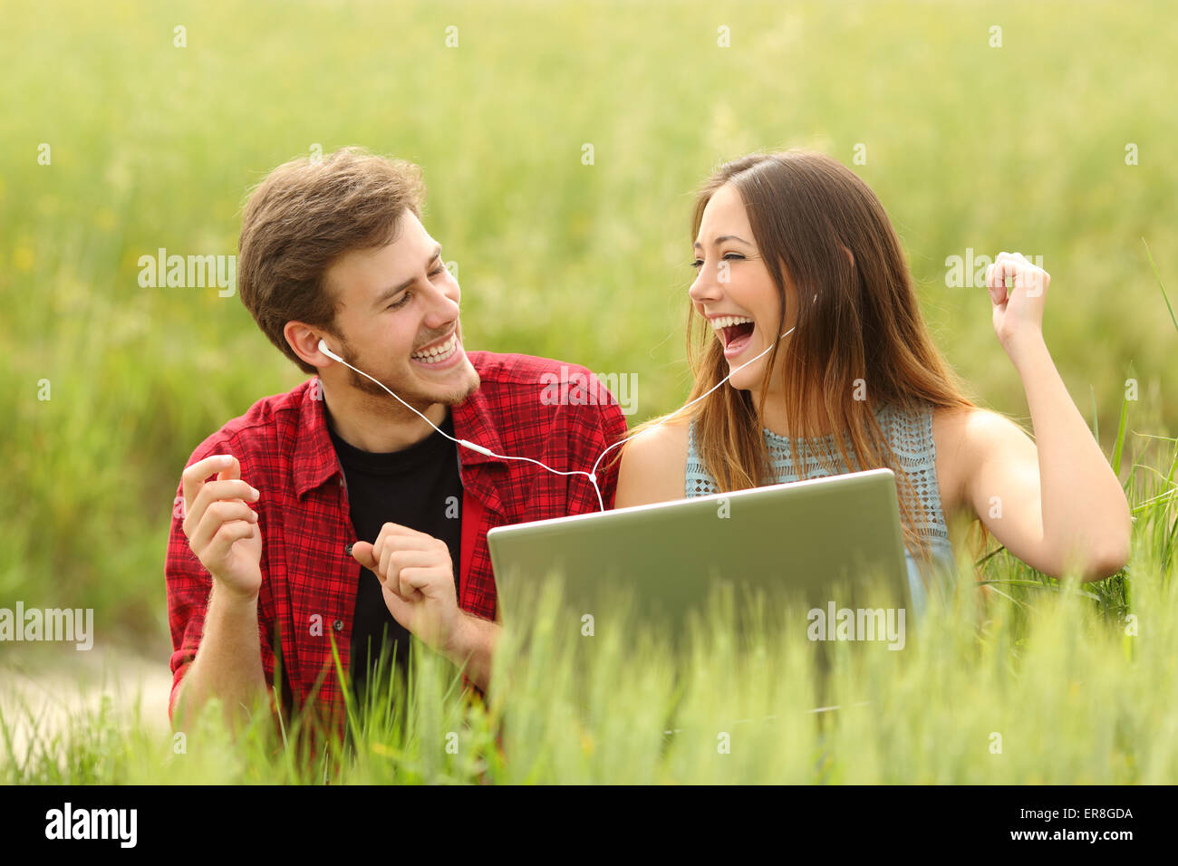 Lustige paar singen und hören von Musik von einem Laptop in einem grünen Feld Stockfoto