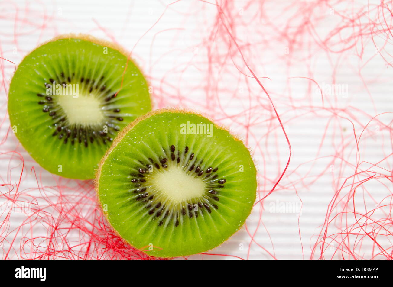 Halbierte Kiwis auf weißem Karton dekoriert mit rosa Stroh Stockfoto