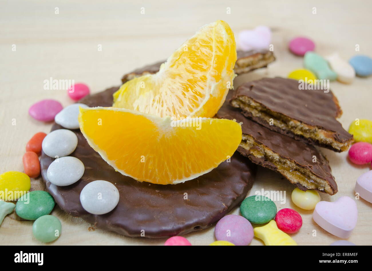 Frische Orange, Kekse und bunte Bonbons auf einem Holztisch Stockfoto
