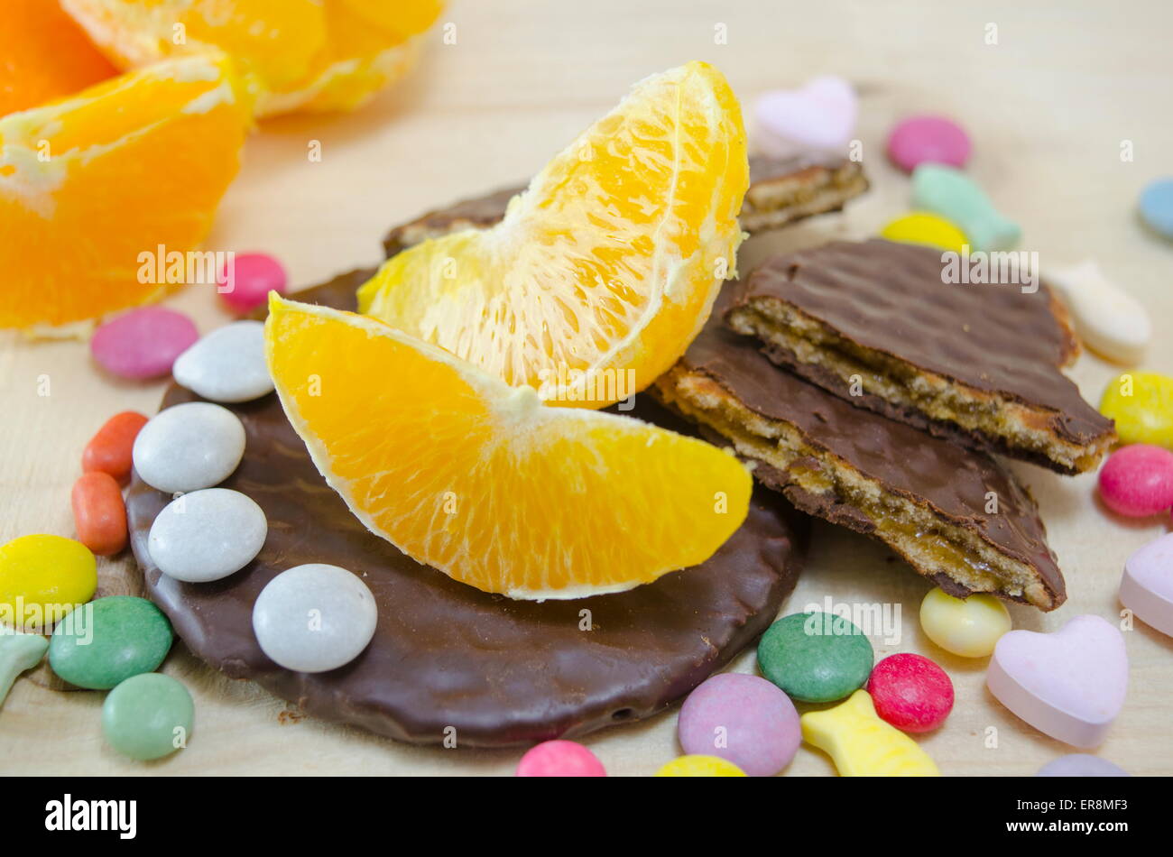 Frische Orange, Kekse und bunte Bonbons auf einem Holztisch Stockfoto