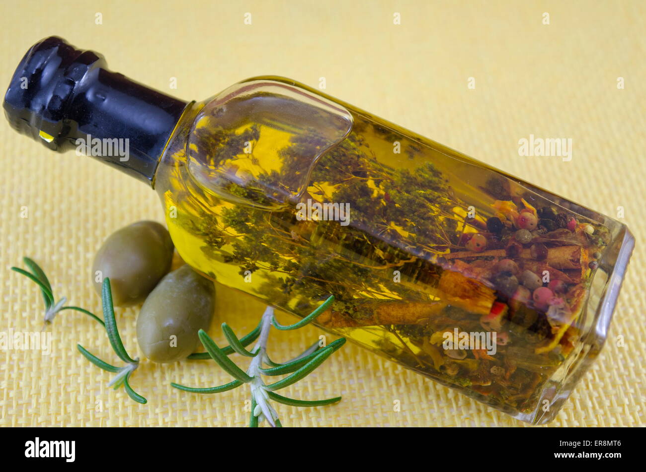 Flasche Olivenöl mit Kräutern innen dekoriert mit frischen grünen Oliven Stockfoto