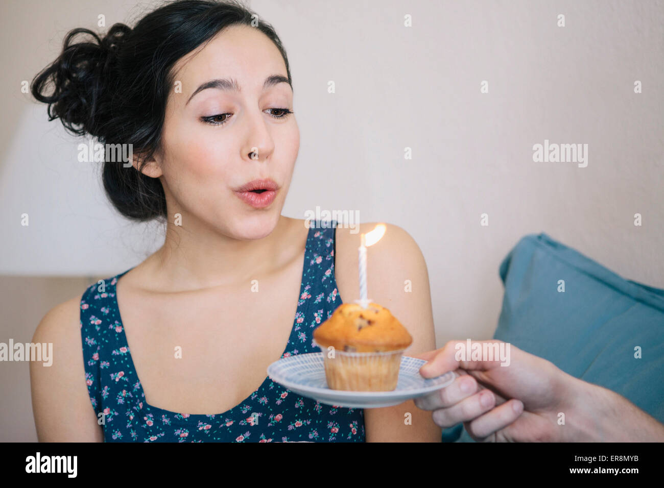 Junge Frau, die Kerze auf Cupcake Ausblasen von Mann zu Hause gehalten Stockfoto