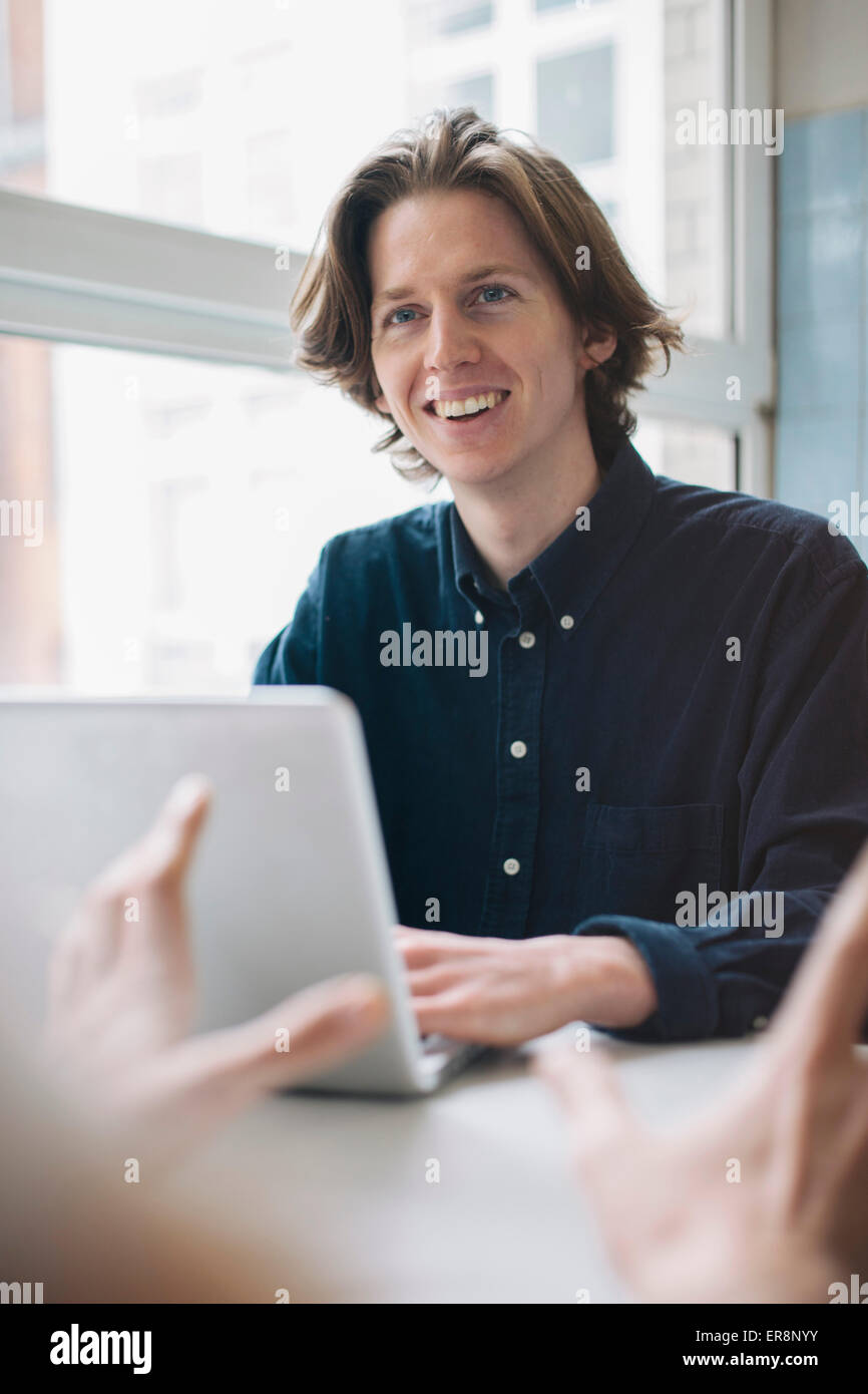 Junger Mann lächelnd an Kollegen während mit Laptop am Tisch Stockfoto
