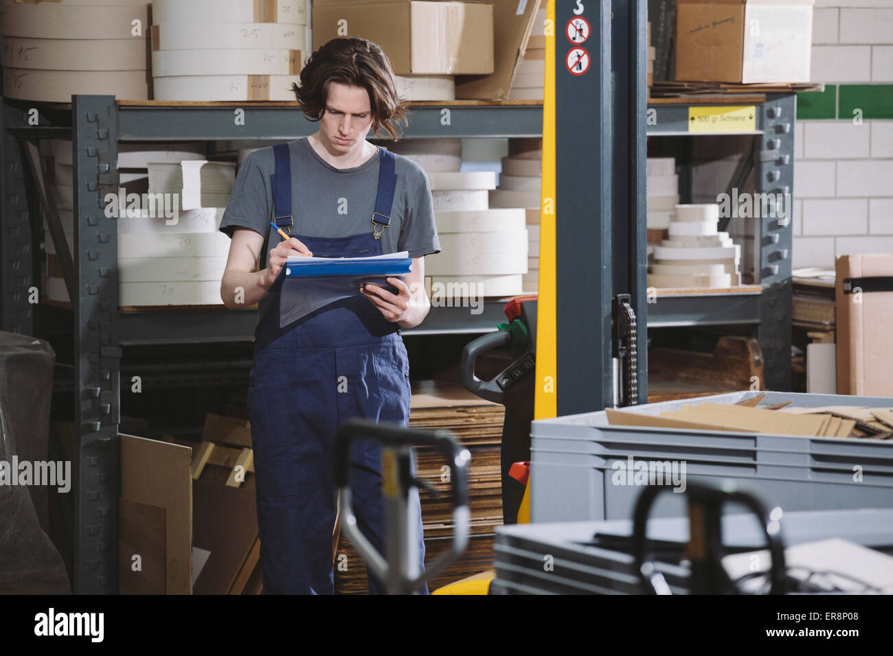 Junge Arbeiter in Overalls Schreiben von Notizen im Lager Stockfoto