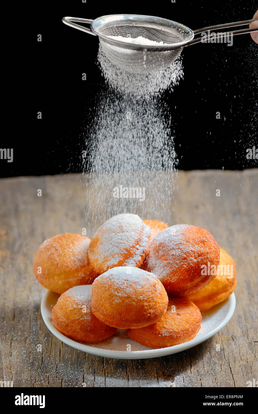 gießt Zucker mit Sieb über donuts Stockfoto