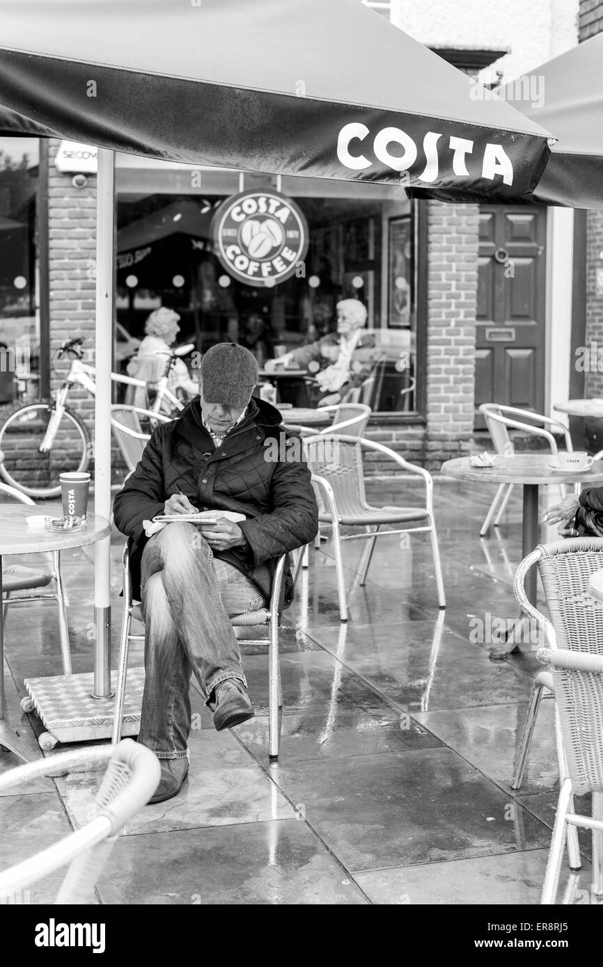 Mann liest eine Zeitung unter einem Dach im Regen im Costa Coffee in Salisbury Stockfoto