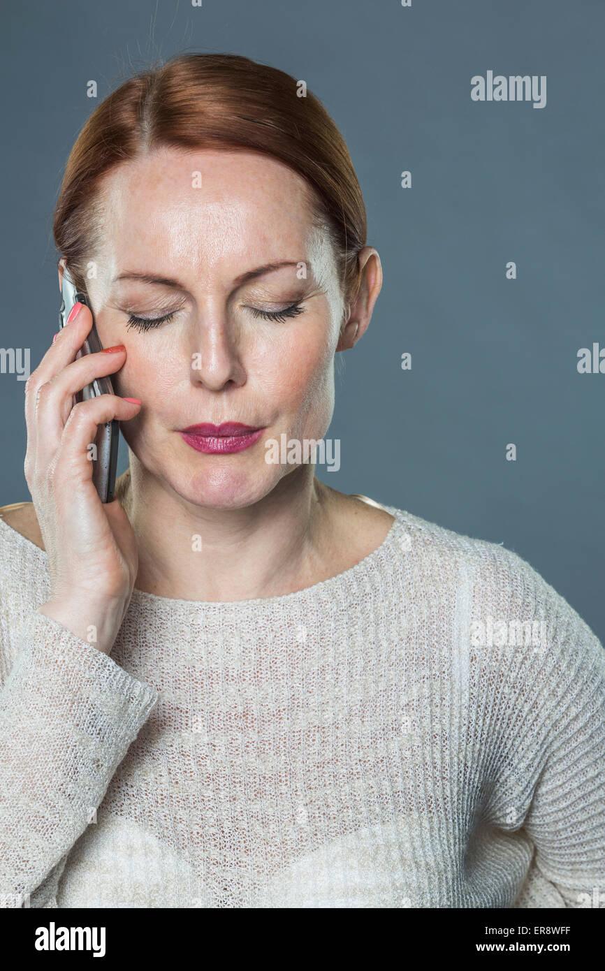 Reife Frau mit Handy vor grauem Hintergrund betont Stockfoto