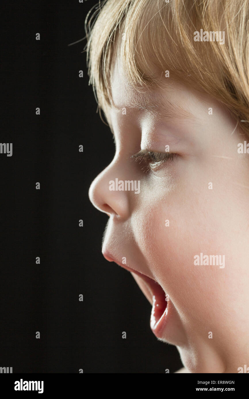 Süsser Boy mit Mund offen vor schwarzem Hintergrund Stockfoto