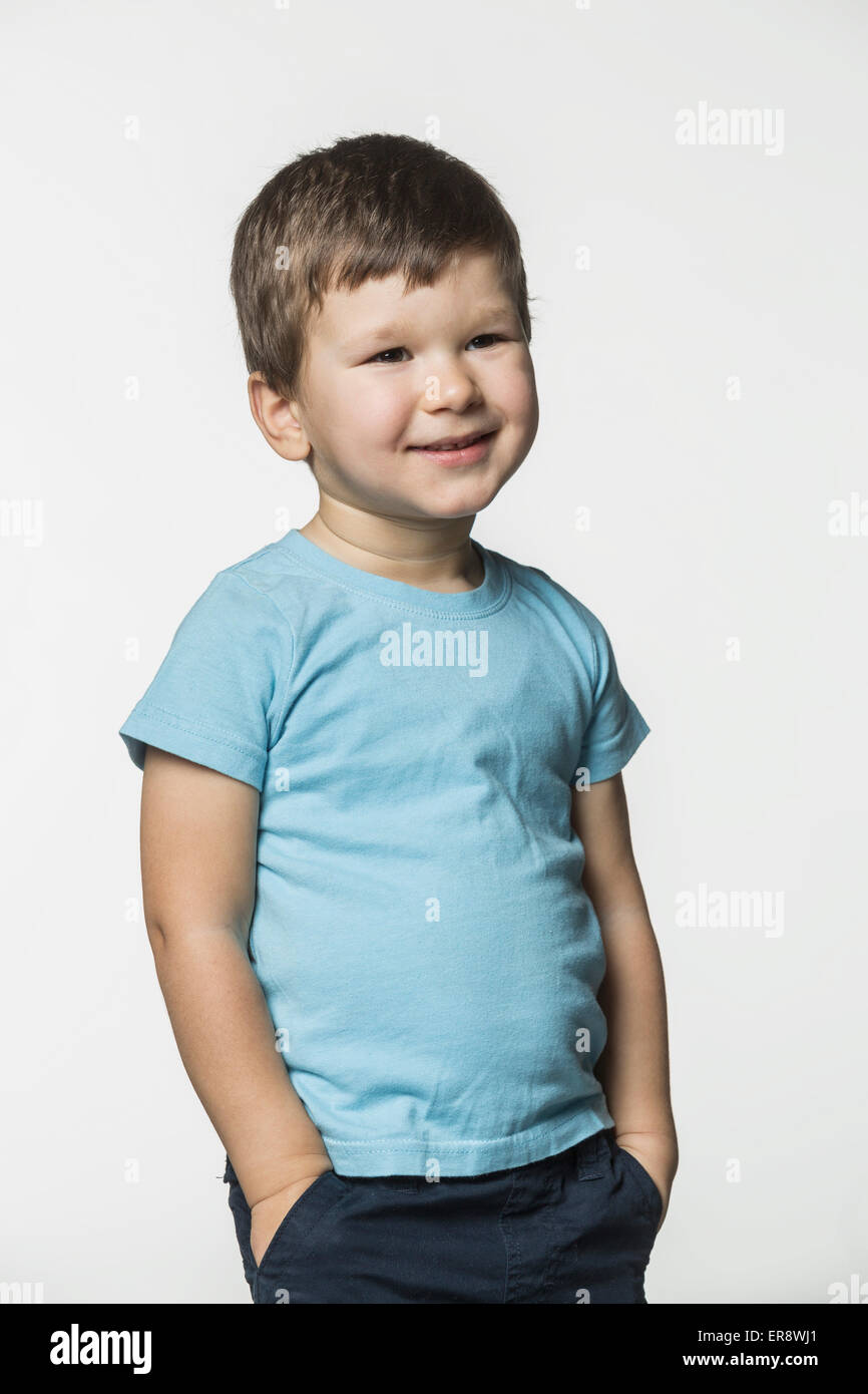 Fröhlicher Junge stehend mit Händen in den Taschen vor weißem Hintergrund Stockfoto