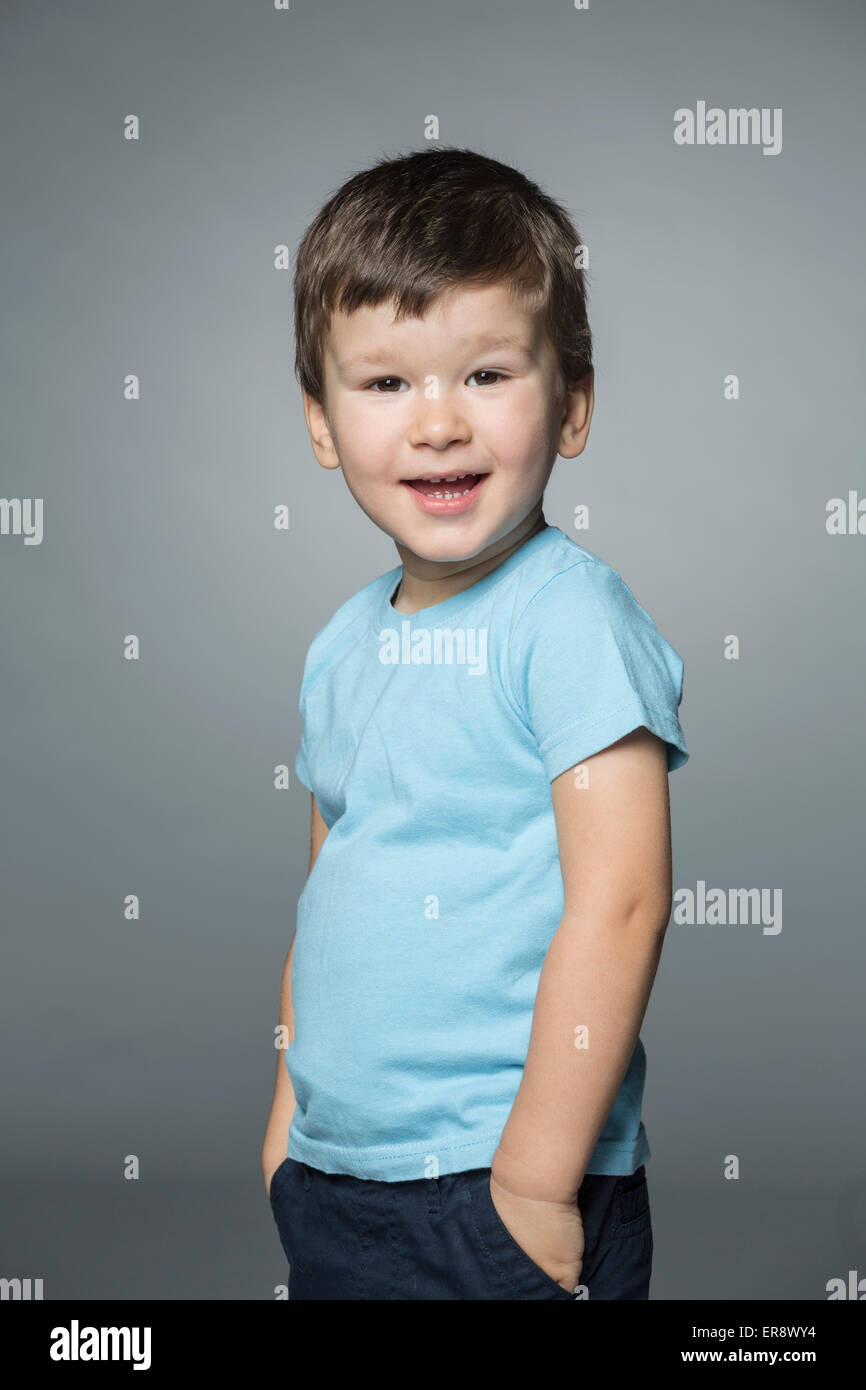Porträt von fröhlicher Junge stehend mit Händen in den Taschen vor grauem Hintergrund Stockfoto