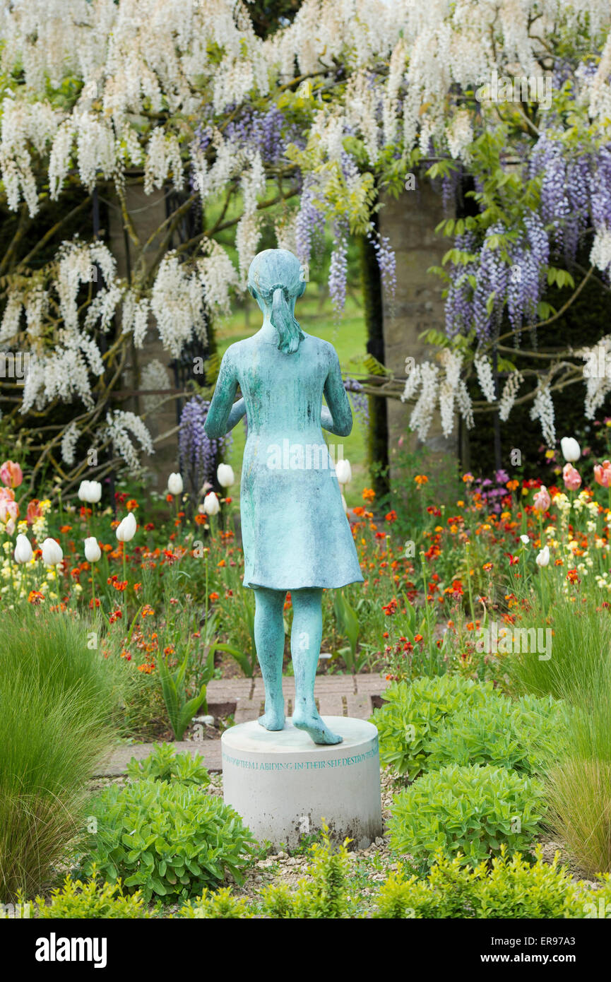 Mädchen-Statue namens "Lampe der Weisheit". Ornamentale Gartenstatue und Glyzinien Torbogen im formalen Garten am Waterperry Gärten, Oxfordshire, Vereinigtes Königreich Stockfoto
