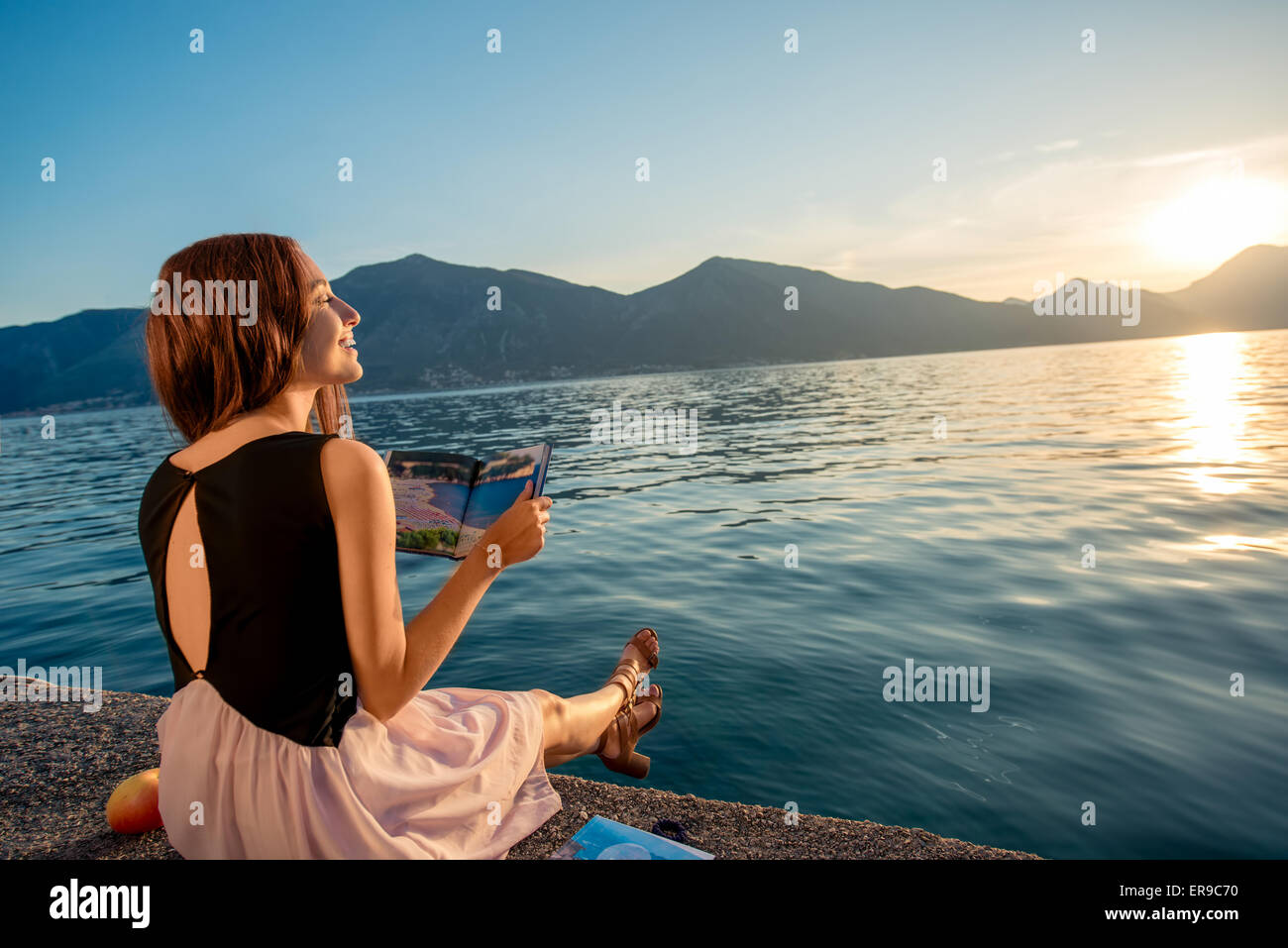Junge Frau sitzt auf dem Pier bei Sonnenaufgang Stockfoto