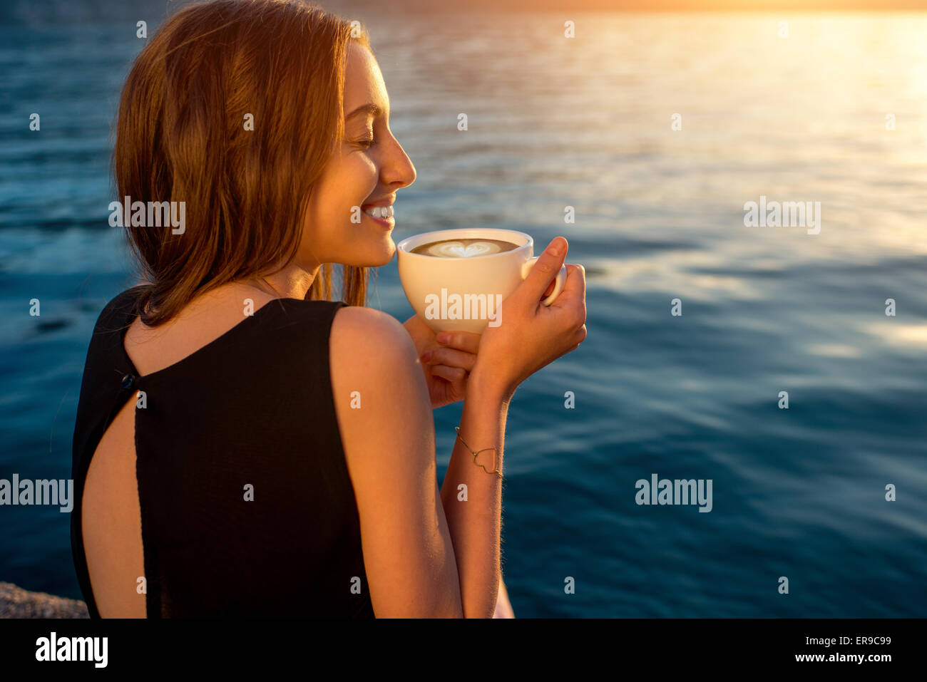 Junge Frau Kaffeetrinken am Pier bei Sonnenaufgang Stockfoto