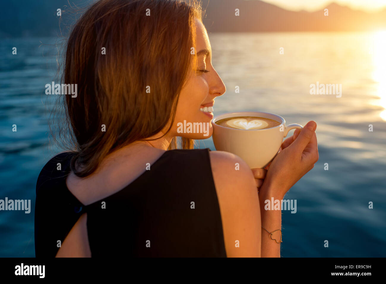 Junge Frau Kaffeetrinken am Pier bei Sonnenaufgang Stockfoto