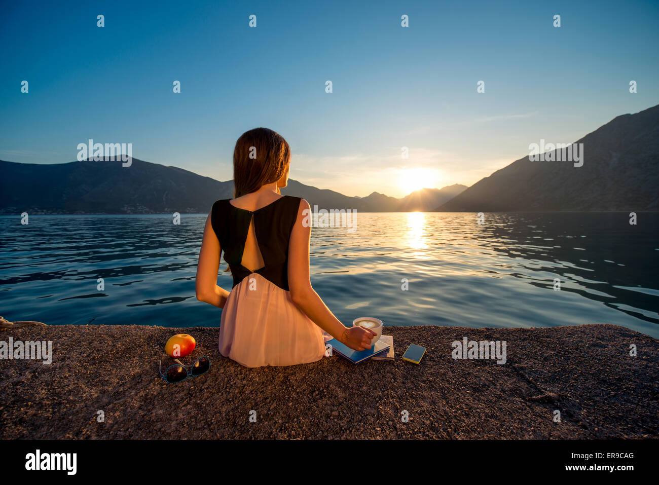 Junge Frau sitzt auf dem Pier bei Sonnenaufgang Stockfoto