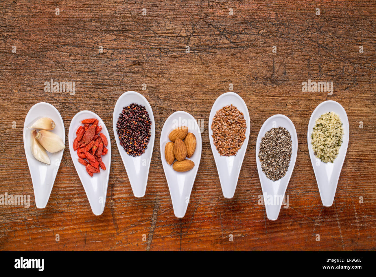 Supernahrungsmittel Getreide, Samen, Beeren, Nüssen und Knoblauch Knoblauchzehen abstrakt - Draufsicht der Löffel Schalen gegen rustikales Holz mit einem Textfreiraum Stockfoto