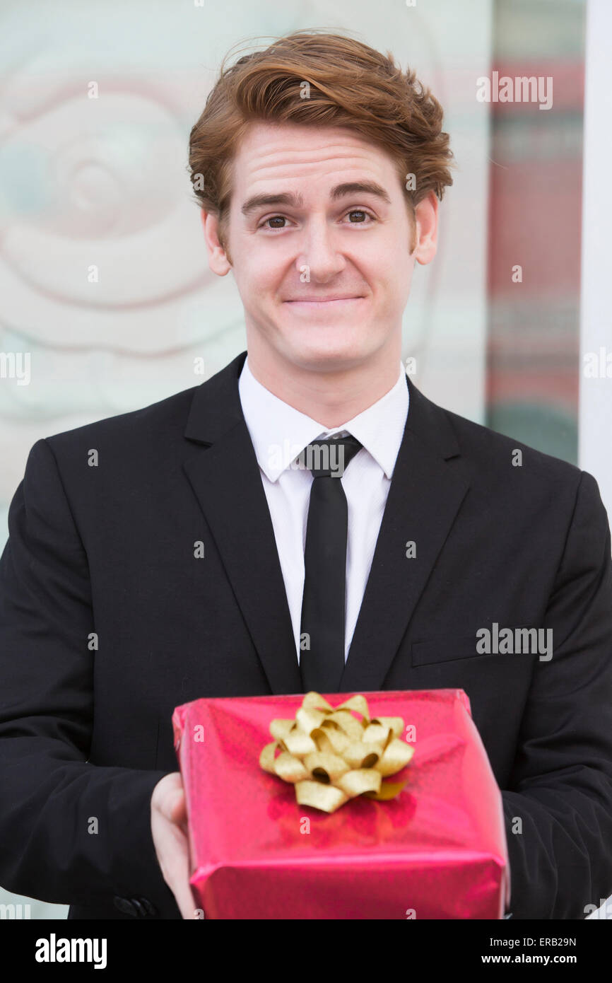 Mann im Anzug hält ein Geschenk in der Hand und einem Lächeln Stockfoto