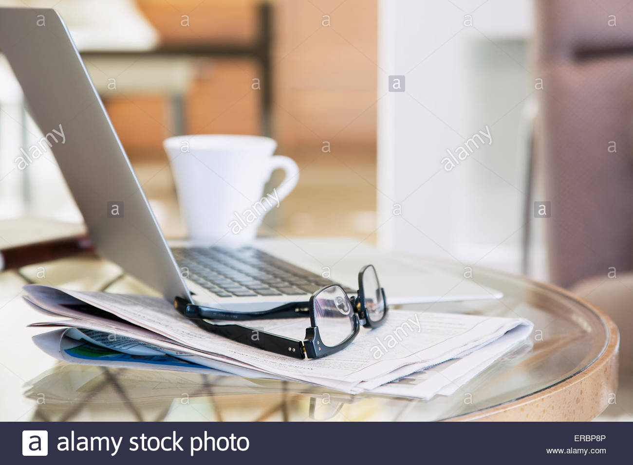 Brillen und Zeitung neben Laptop und Kaffee Stockfoto