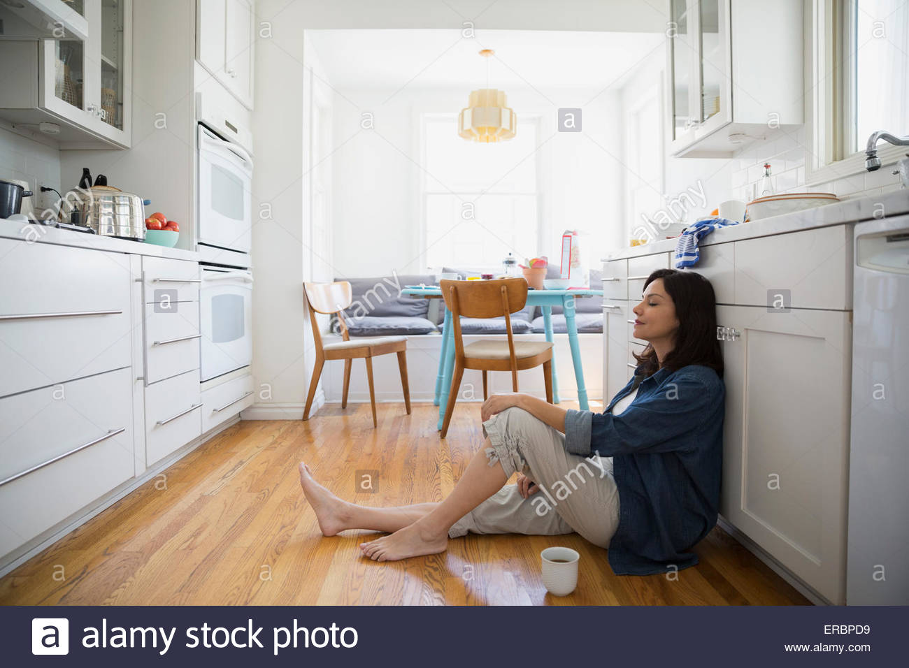 Heitere Brünette Frau sitzt Küche Boden Augen geschlossen Stockfoto