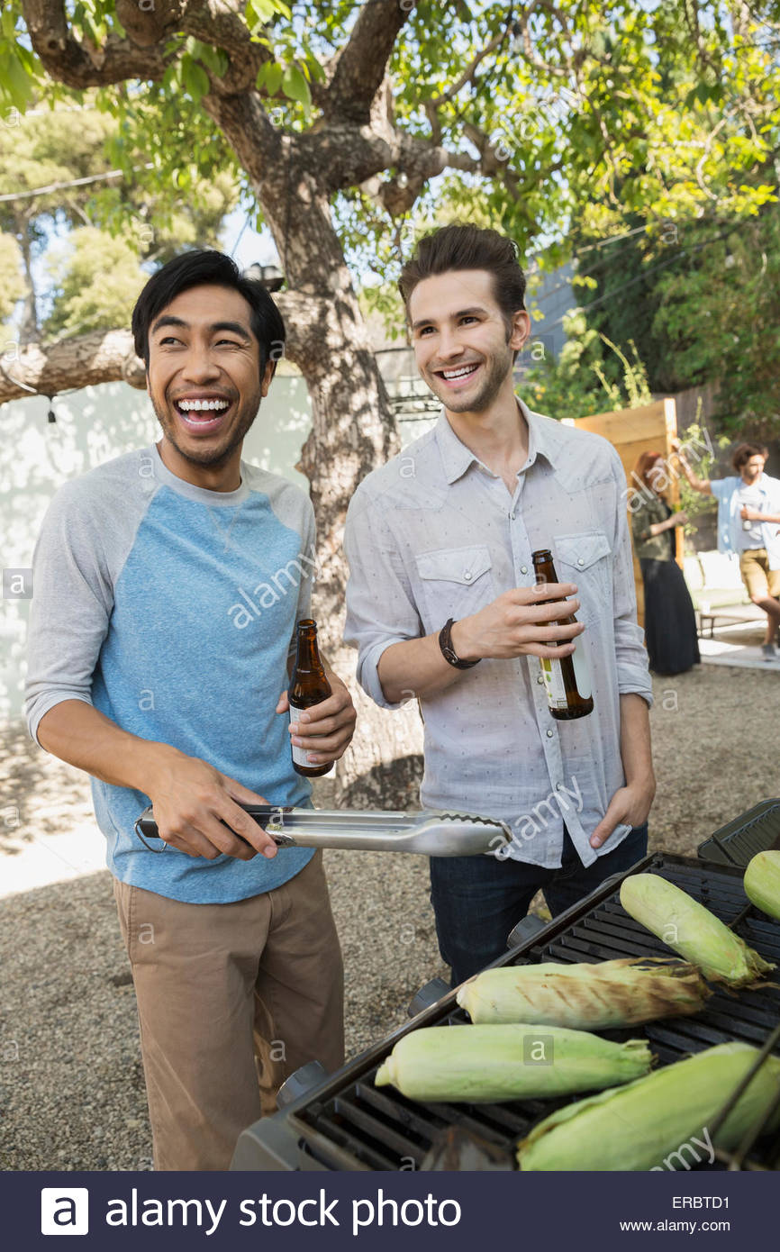 Lächelnde Männer Bier trinken und Grillen Maiskolben Stockfoto
