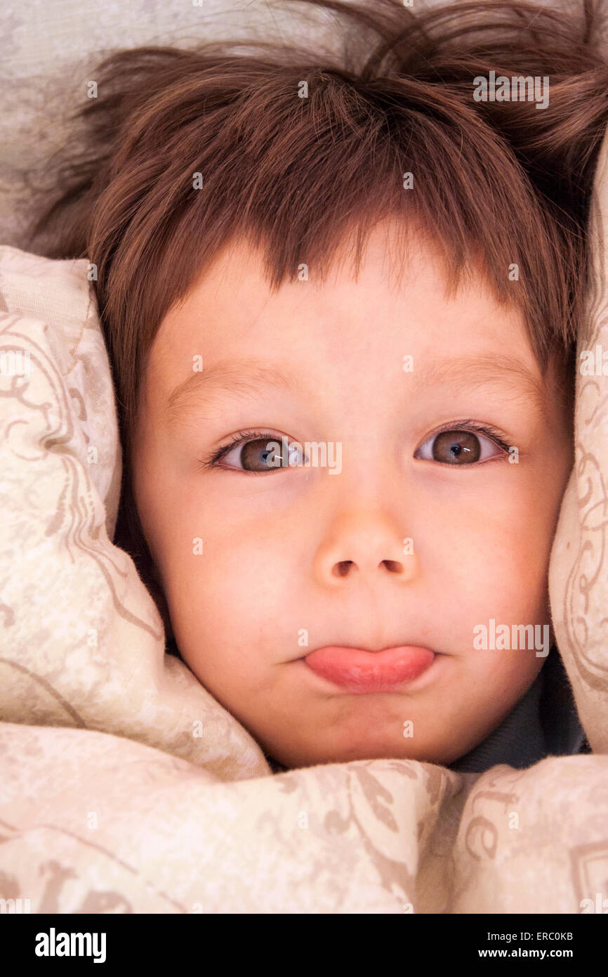 Nahaufnahme des Gesichts des Kleinkindes, Jungen, 3-4 Jahre alt, braune Haare. Kuschelte sich im Bett mit Bettdecke um das Gesicht, als er herausguckt. Während des Poutierens. Stockfoto