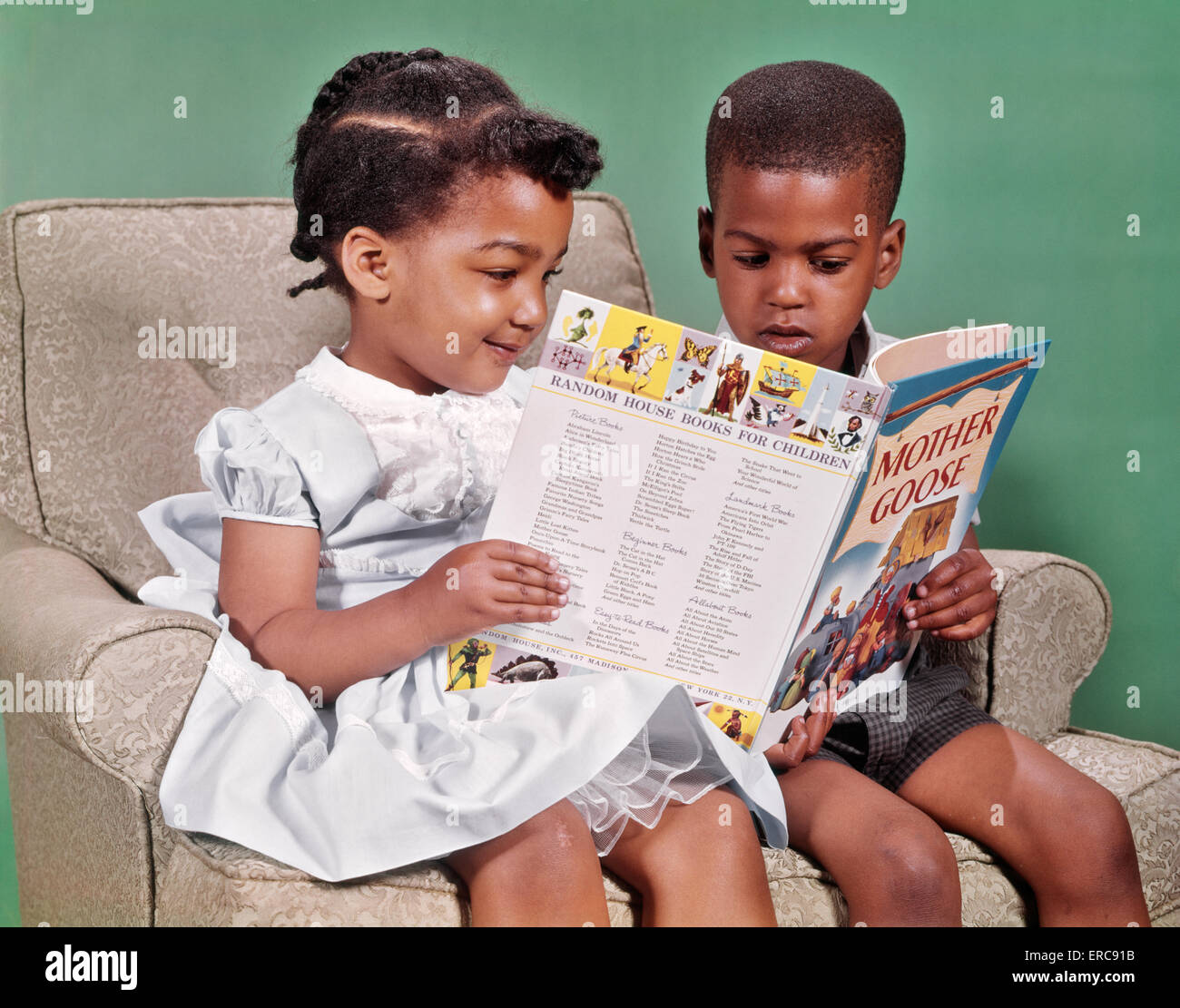 1960ER JAHREN AFRIKANISCHE AMERIKANISCHE JUNGEN UND MÄDCHEN SITZEN IM SESSEL LESEBUCH VON MUTTER GANS REIME Stockfoto