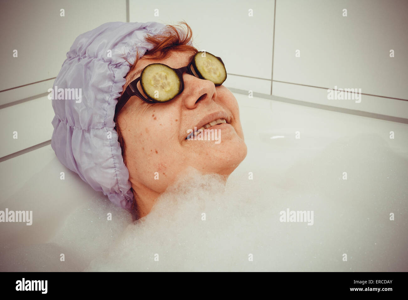 Reife Frau in der Badewanne mit Gurkenscheiben auf Brillen, Retro-Stil Stockfoto