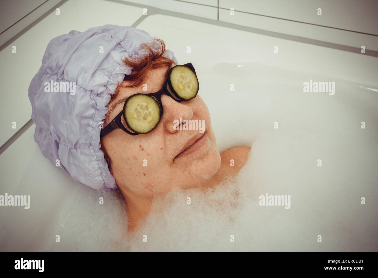 Reife Frau in der Badewanne mit Gurkenscheiben auf Brillen, Retro-Stil Stockfoto
