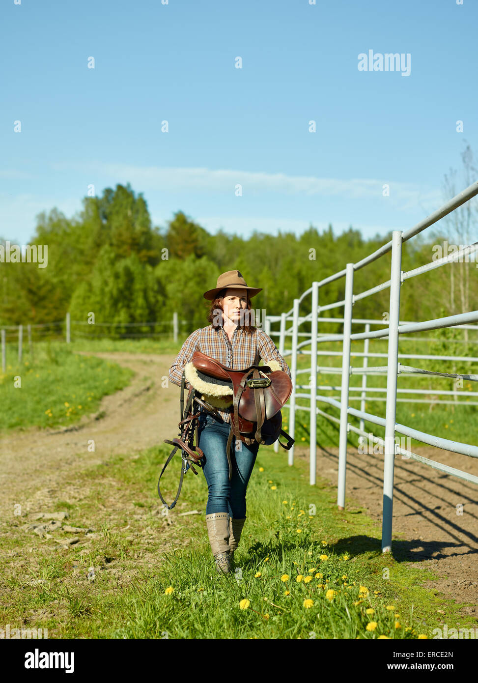 Cowgirl trägt einen Sattel, und sie wandern entlang des Fahrerlagers Stockfoto