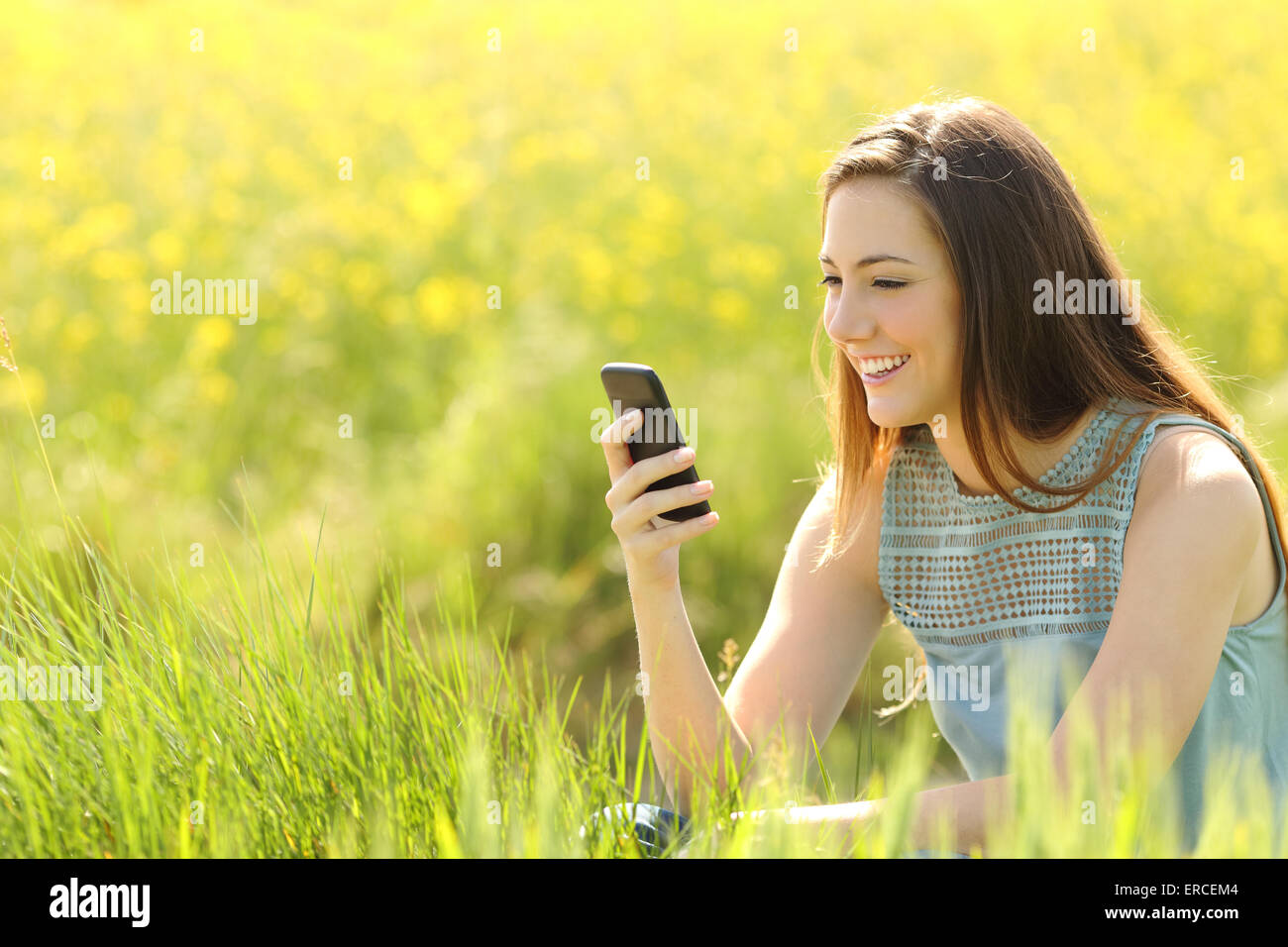 Frau mit einem smart-Phone in einem grünen Feld mit gelben Blüten im Sommer Stockfoto