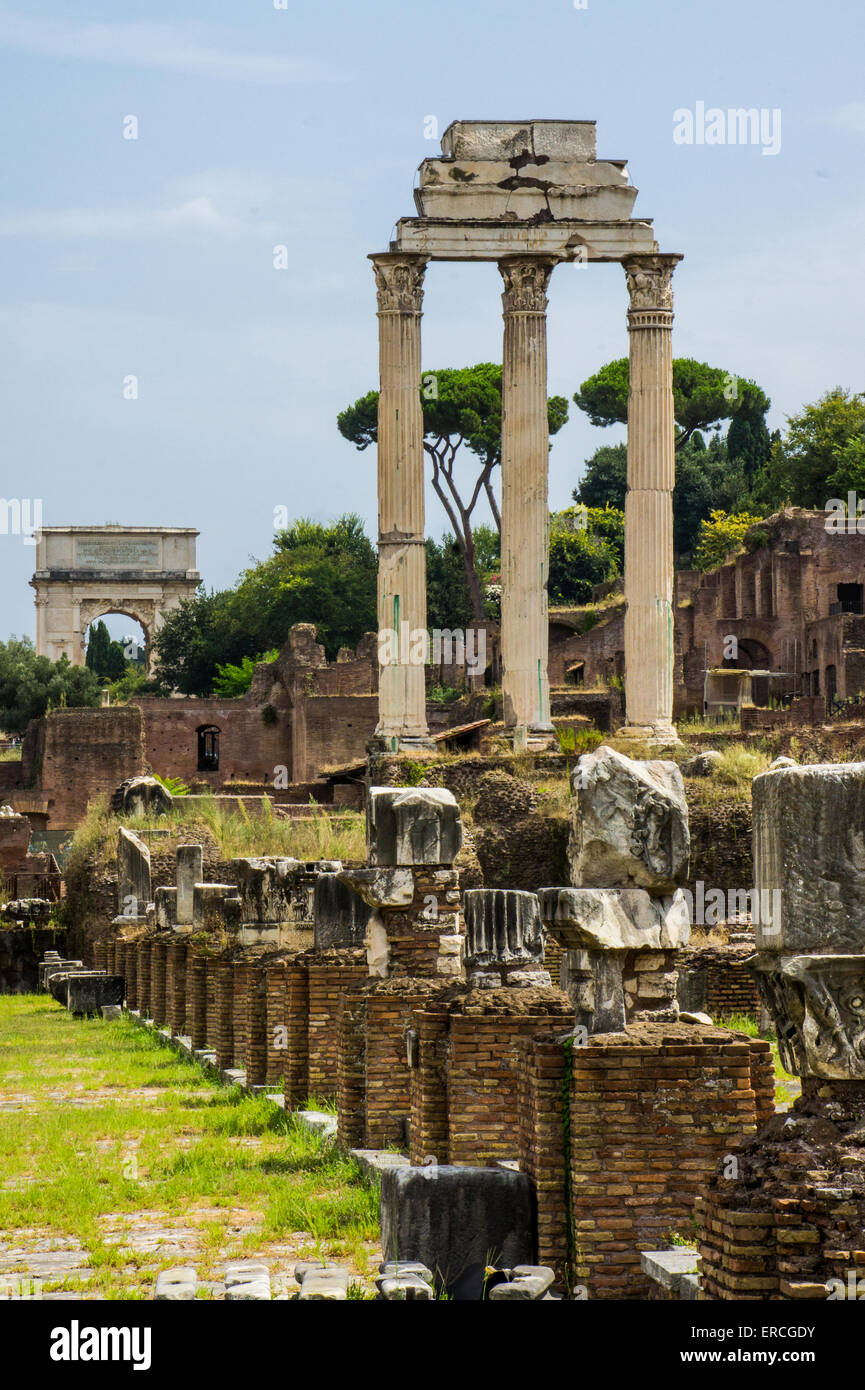 Drei Spalten bleiben aus dem Tempel des Castor und Pollux auf dem Forum Romanum in Rom. Bogen von Titus im Hintergrund. Stockfoto