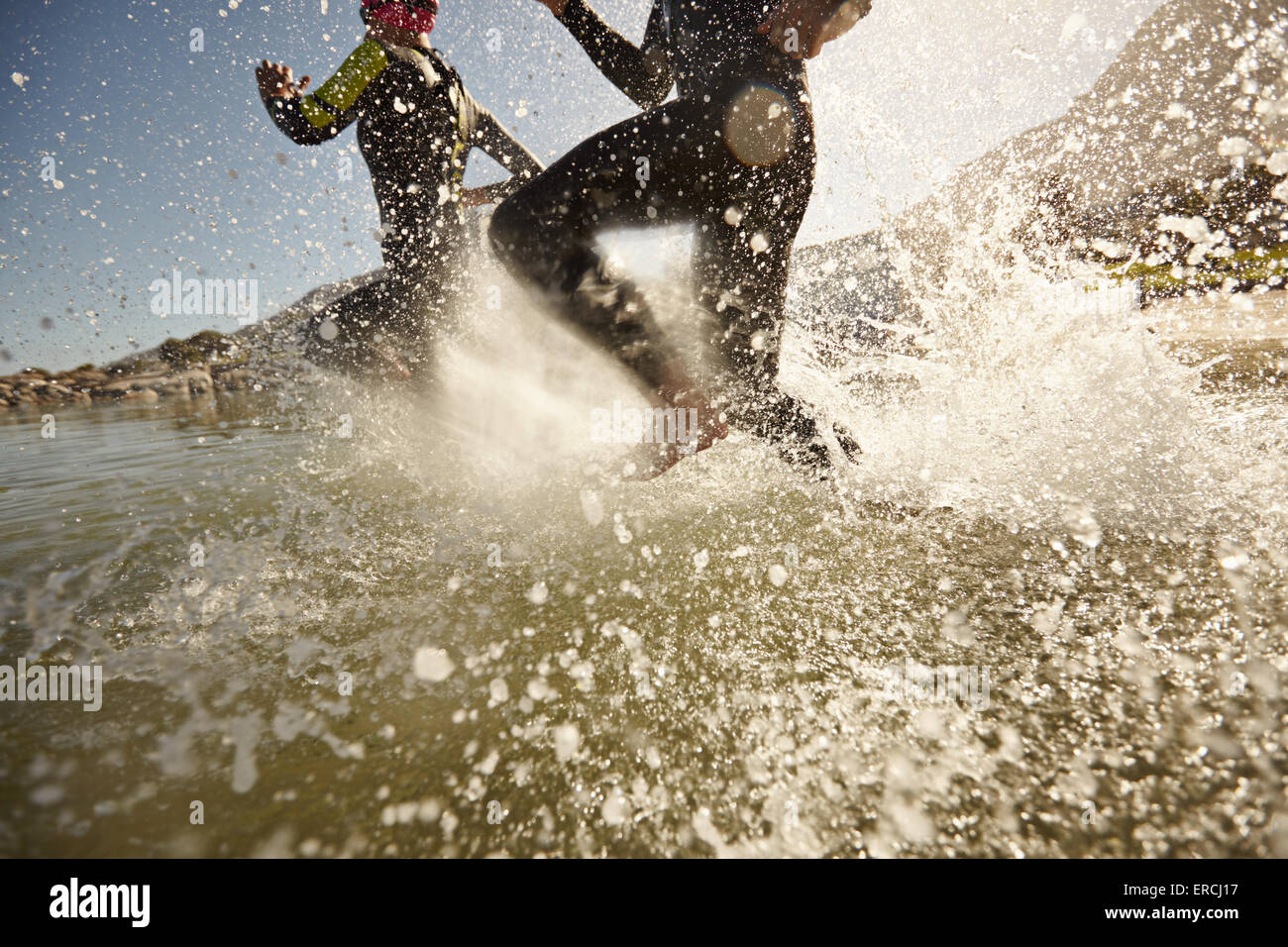 Zwei Triathlon-Teilnehmer laufen in das Wasser zum Schwimmen Teil des Rennens. Spritzer Wasser und Athleten laufen. Wasser im Fokus Stockfoto